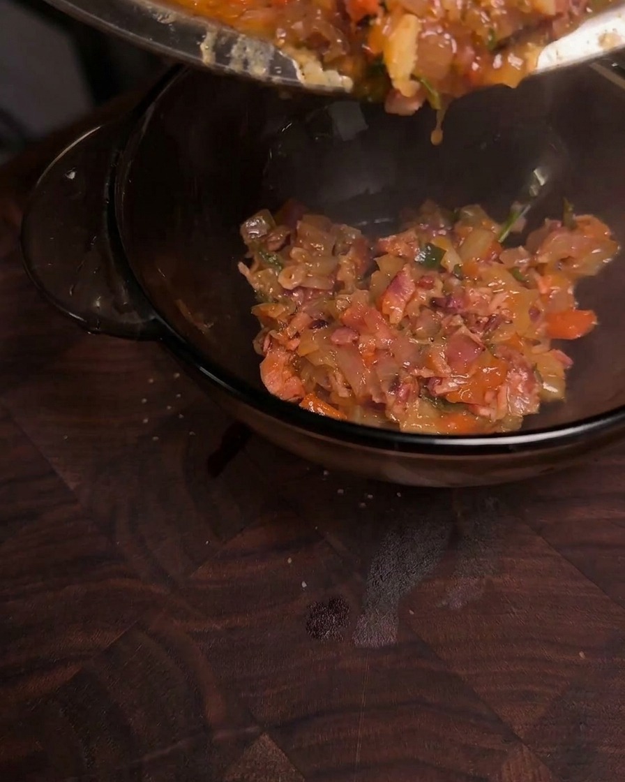 Una densa e lucida confettura di bacon caramellata viene versata da una padella in una ciotola di vetro trasparente.