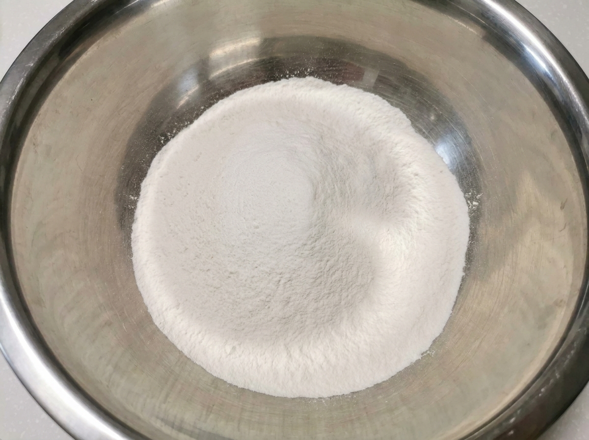 Un cumulo bianco e incontaminato di farina di riso e farina 00 mescolate allinterno di una grande e pulita ciotola di acciaio inox.