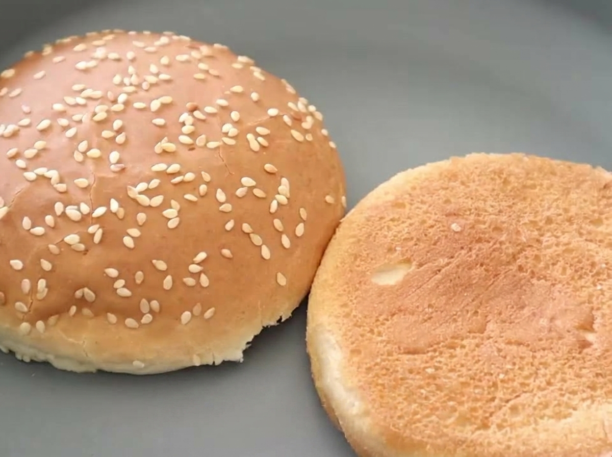 Due metà di un panino con semi di sesamo per hamburger viste fianco a fianco, con una che rivela un interno tostato e dorato.
