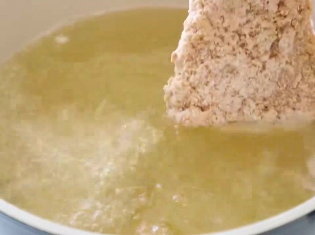 Un filetto di pollo panato immerso in una pentola di olio per frittura bollente e scintillante.