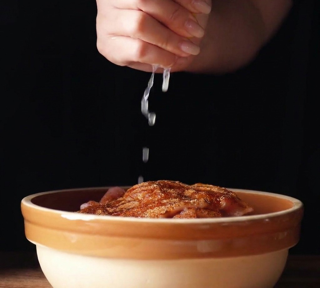 Succo di limone fresco spremuto da uno spicchio sopra le sovracosce di pollo condite in una ciotola di ceramica.