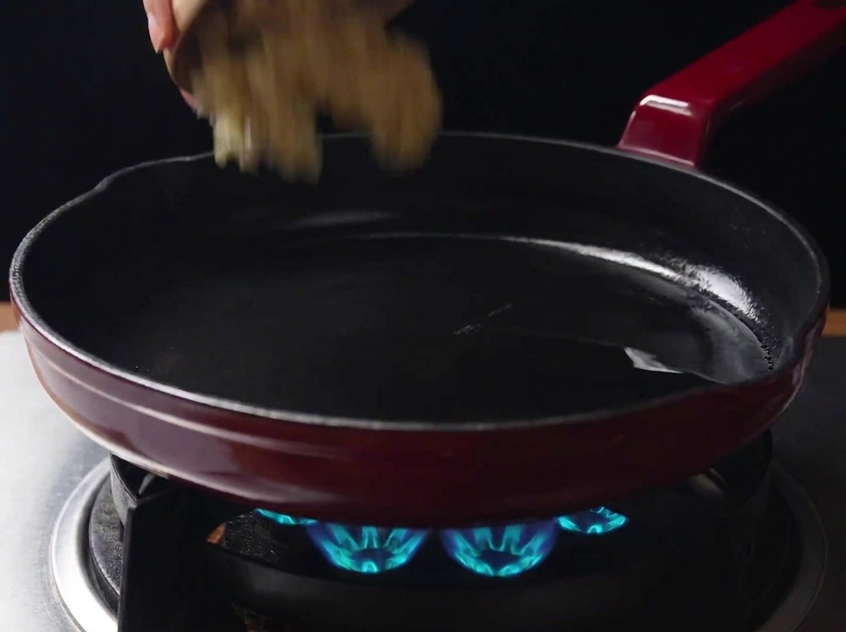 Aglio tritato aggiunto da una ciotolina in una padella calda con olio su un fornello a gas acceso.