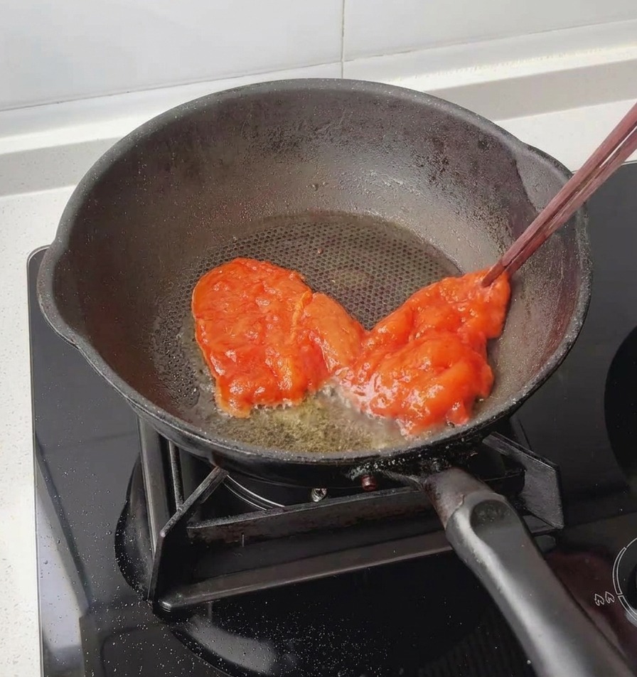 Delle bacchette utilizzate per adagiare un petto di pollo rosso completamente marinato in una padella nera leggermente unta.