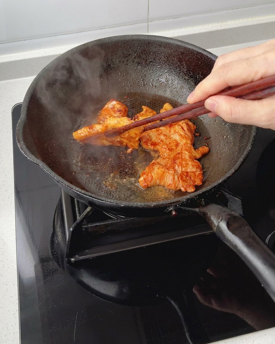 Pezzi di petto di pollo marinato che rosolano in padella mentre vengono girati con delle bacchette, mostrando una golosa glassatura caramellata.
