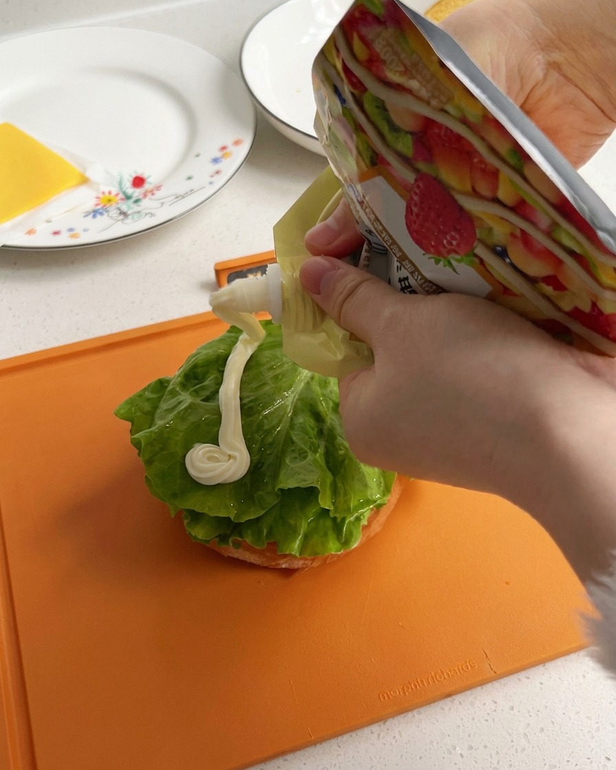 Maionese bianca e cremosa che viene spremuta formando una linea spessa sopra una foglia di insalata verde sulla base del panino.