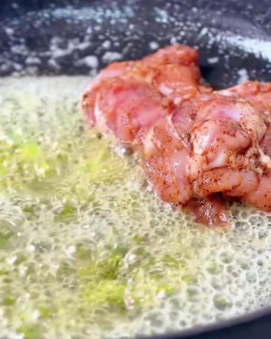 Cosce di pollo Cajun marinate che sfrigolano in padella immerse in unabbondante quantità di burro fuso spumeggiante.