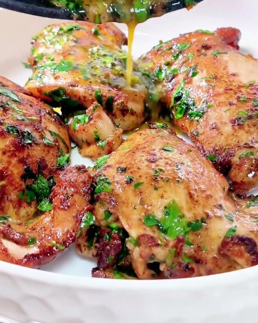 Un filo di salsa lucida al burro dorato ed erbe aromatiche versato da una padella sopra succulente cosce di pollo dorate in una ciotola bianca pulita.
