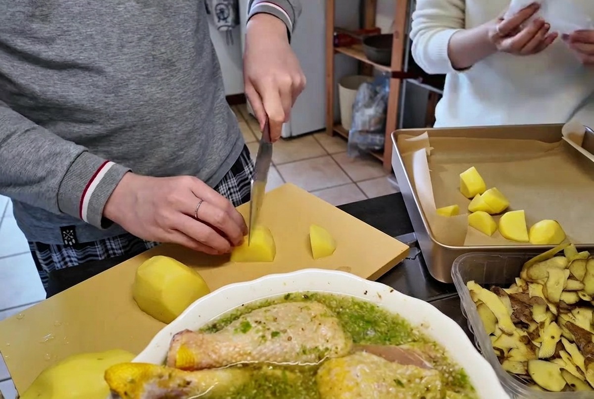 Taglio di patate crude pelate a pezzi della dimensione di un boccone su un tagliere usando un coltello da cucina affilato.