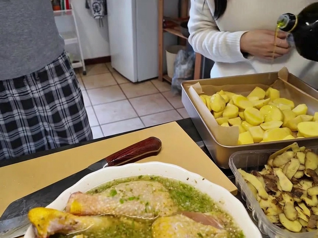 Versare olio doliva da una bottiglia di vetro su una teglia piena di patate tagliate a pezzi.