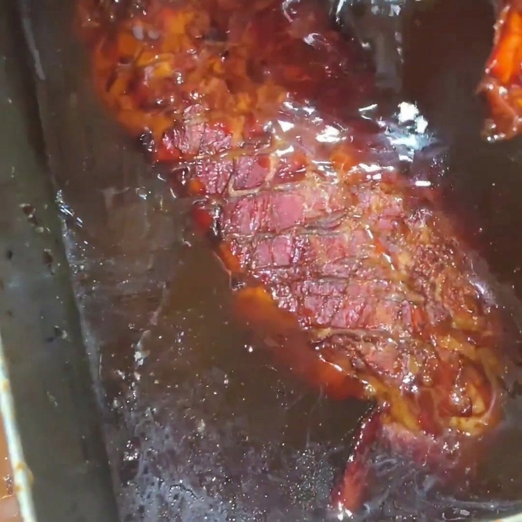 Un pezzo di costine di maiale arrostito e dorato che viene cosparso con un ricco e lucido sciroppo di miele allinterno di un vassoio in acciaio inossidabile.
