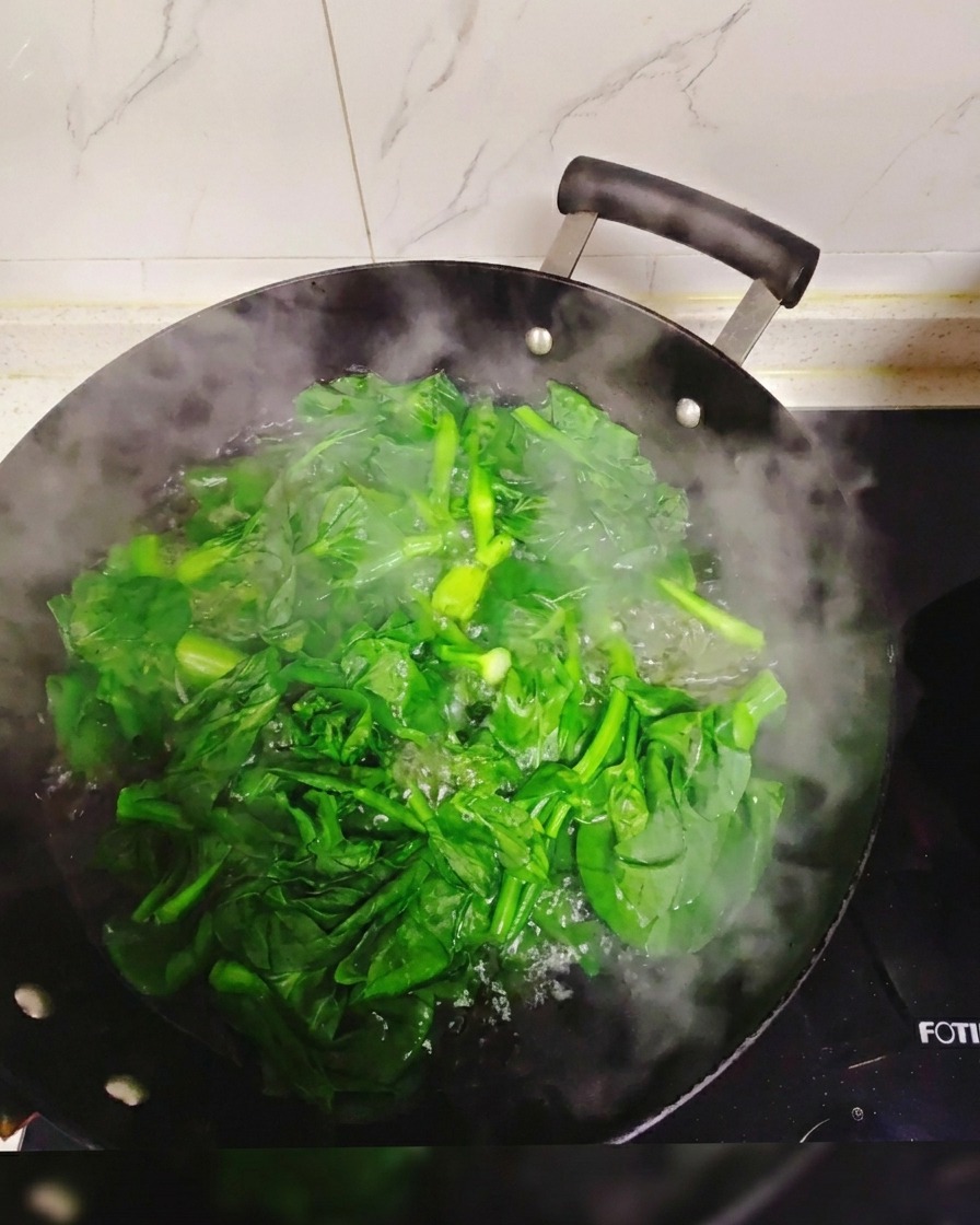 Verdure fresche a foglia verde immerse e sbollentate in un grande wok pieno di acqua bollente e fumante.