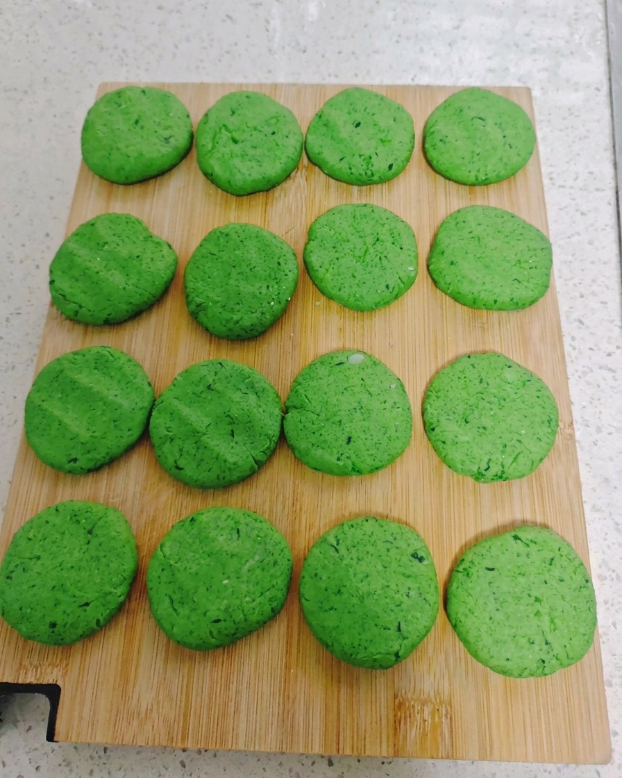 Sedici pancake rotondi alle verdure disposti in modo ordinato su un tagliere di legno.