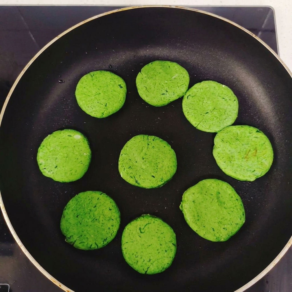 Diversi pancake rotondi alle verdure disposti in cerchio allinterno di una padella antiaderente nera prima della cottura.