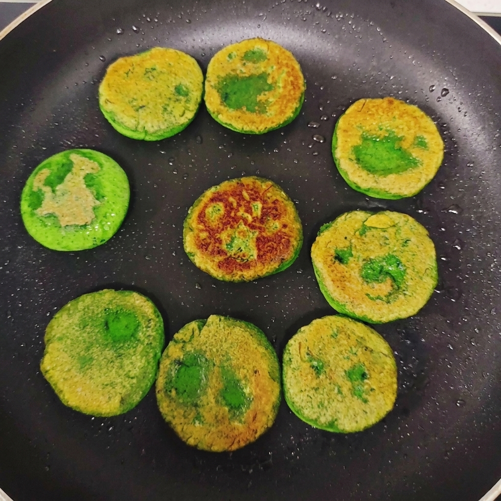Pancake verdi alle verdure girati in padella, che mostrano una crosticina dorata non uniforme sulla superficie.