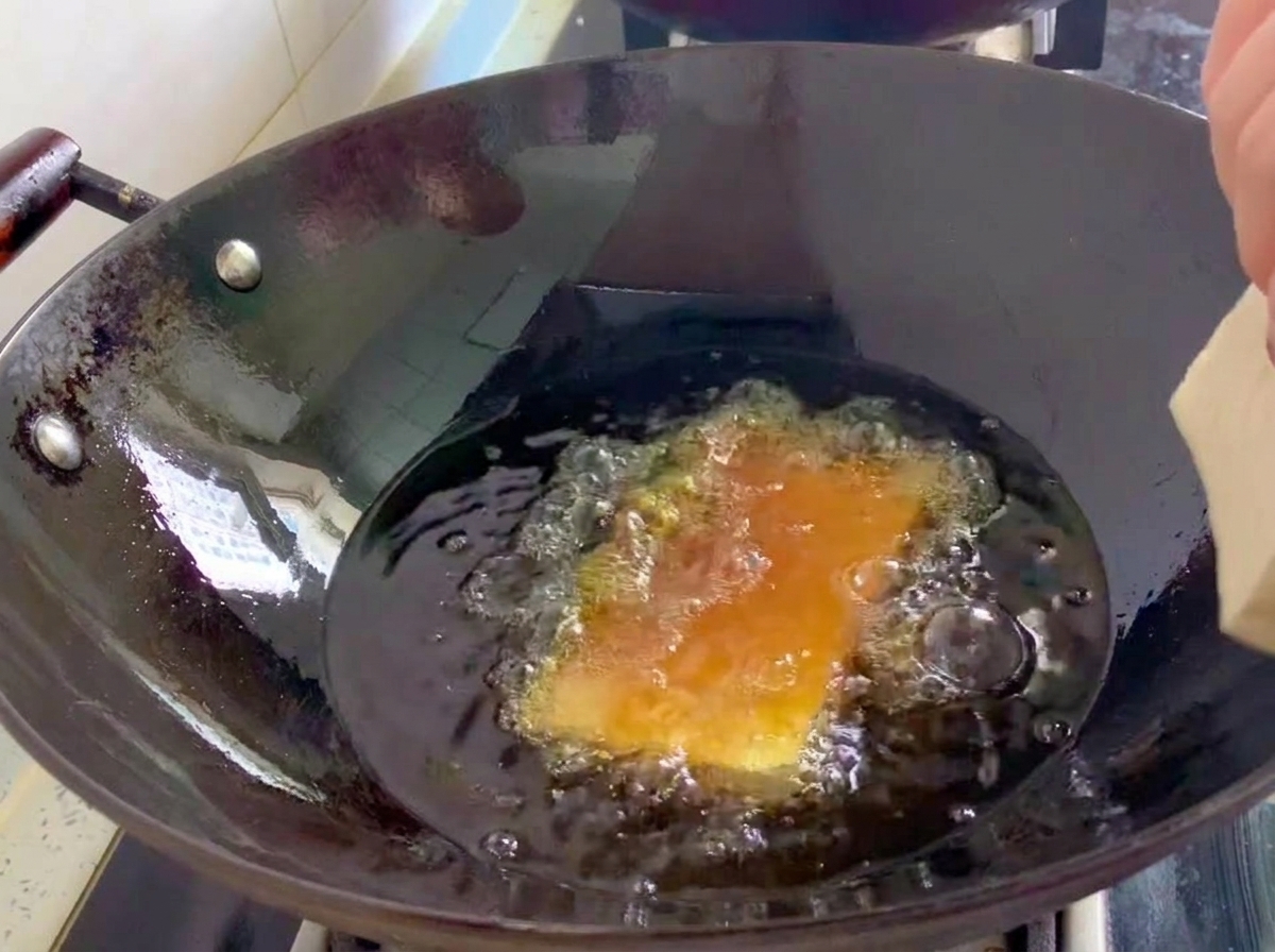 Pezzi di tofu sodo che friggono in un wok pieno di olio bollente.