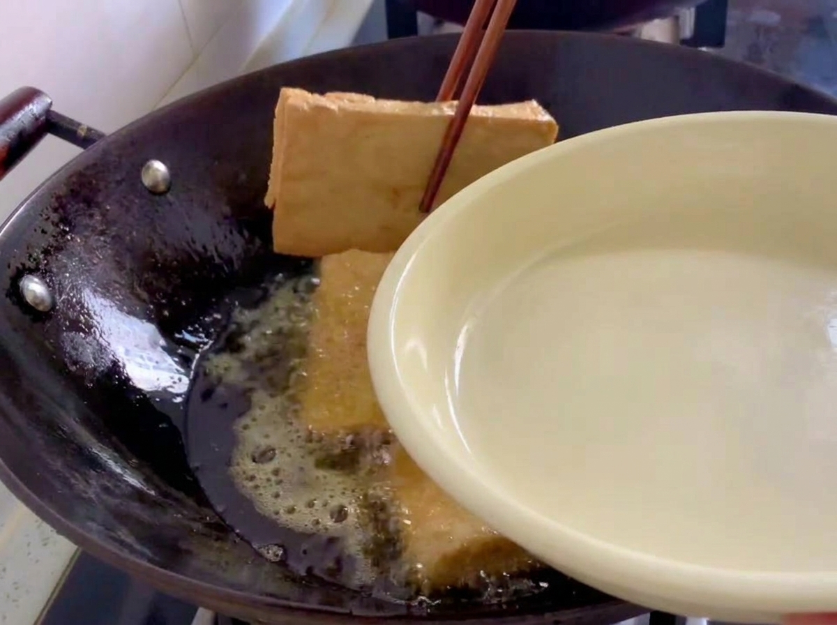 Blocchi di tofu fritto ben dorati sollevati da un wok con delle bacchette di legno.