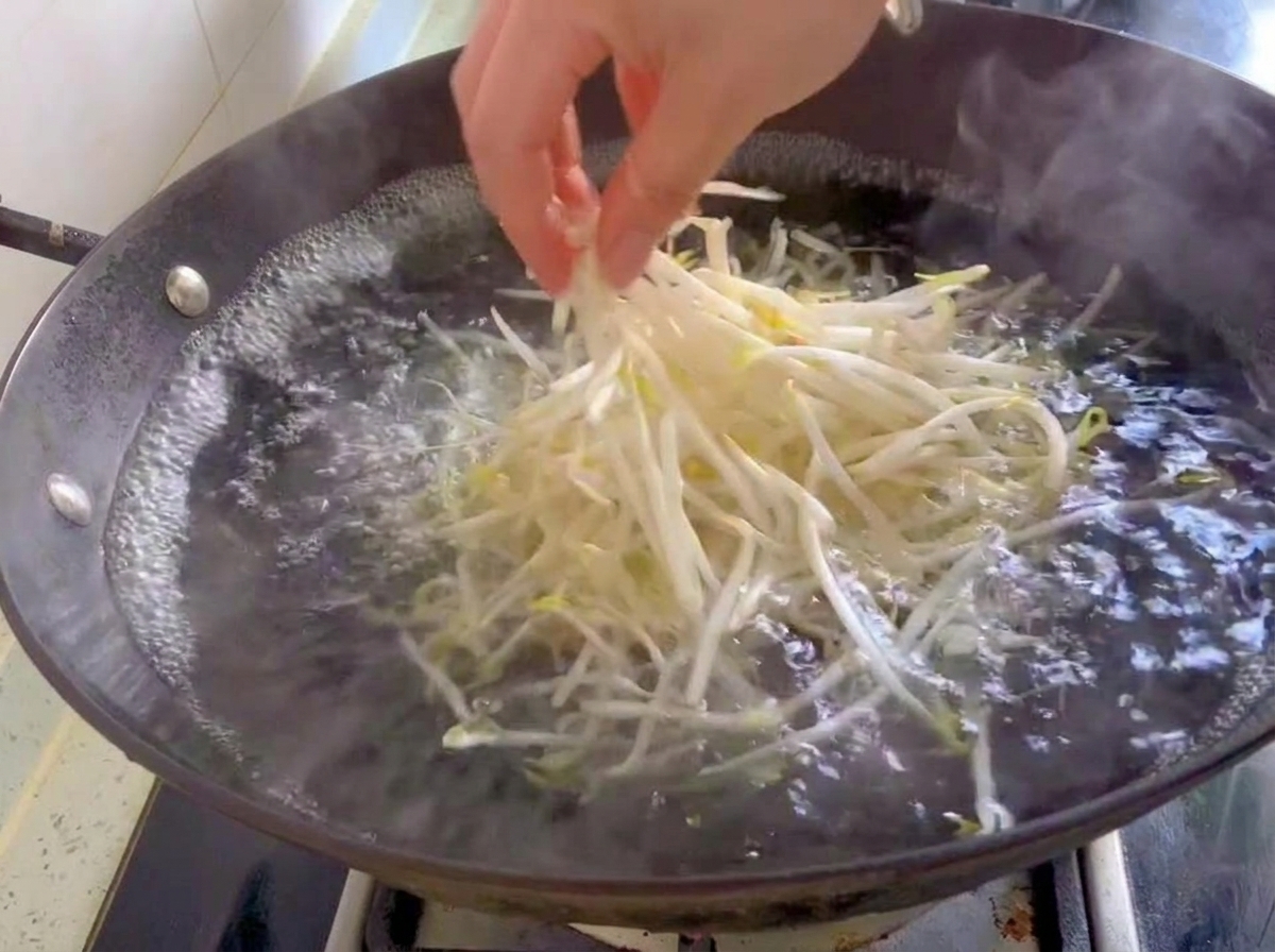 Una manciata di germogli di soia freschi e bianchi gettati in un wok con acqua in ebollizione.