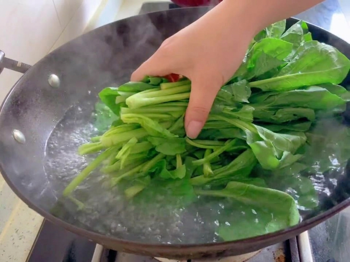 Un mazzo di foglie fresche di spinaci verdi immerso nellacqua bollente di un wok.