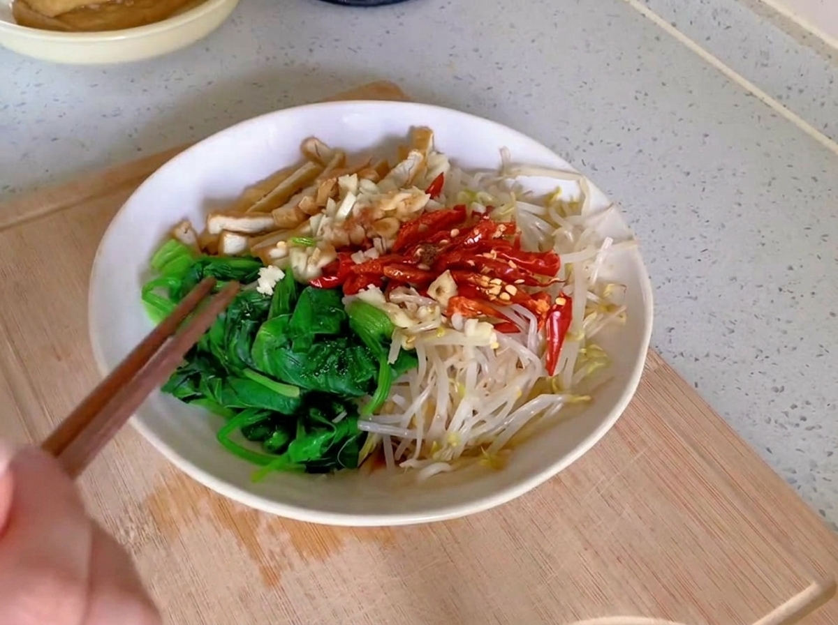 Un paio di bacchette di legno che mescolano un mix di spinaci verdi, germogli di soia chiari, strisce di tofu e peperoncini rossi in una ciotola di ceramica bianca.
