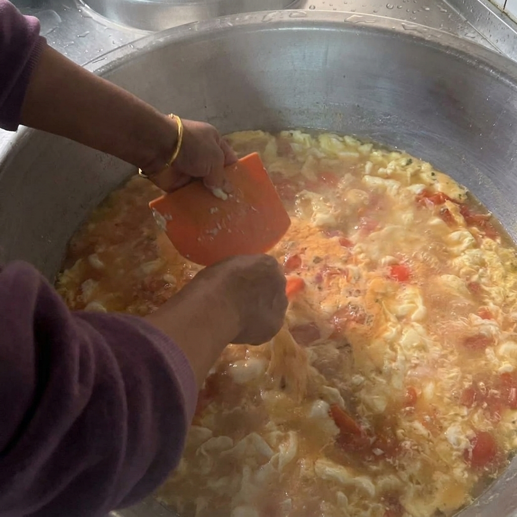 Mani che impugnano un tarocco di plastica arancione per far cadere piccoli pezzi di impasto molle in una grande pentola di zuppa di pomodoro bollente.