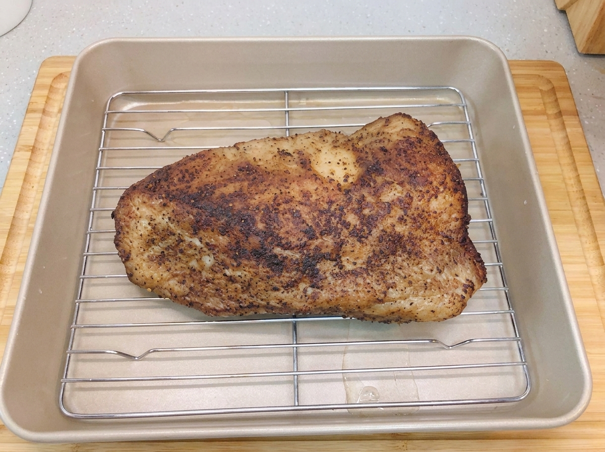Il brisket adagiato sulla griglia allinterno della teglia dorata, sul cui fondo è stato versato un sottile strato dacqua.