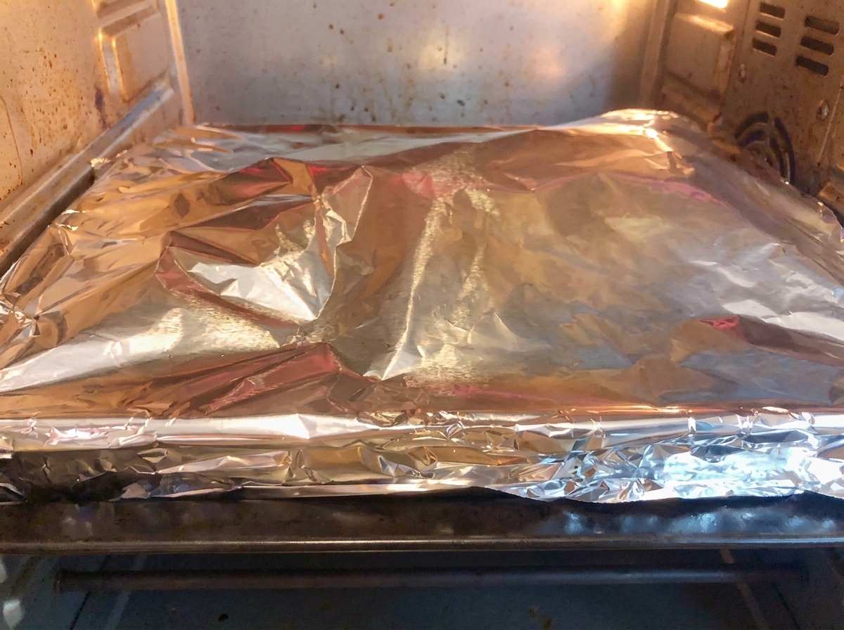 La teglia coperta dallalluminio posizionata nel forno di casa per la cottura a bassa temperatura.