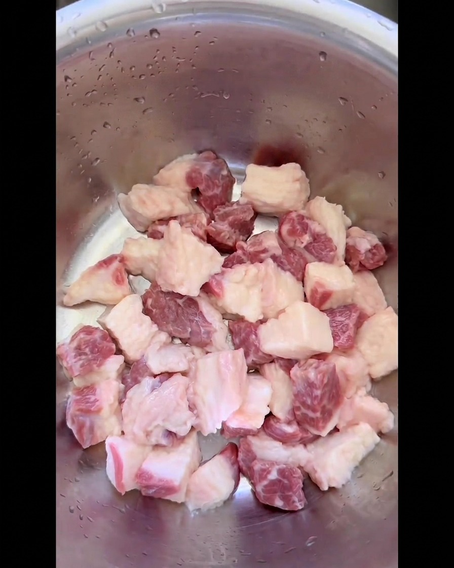 Pezzi grezzi di grasso di punta di petto di manzo tagliati in cubetti uniformi allinterno di una ciotola di acciaio.