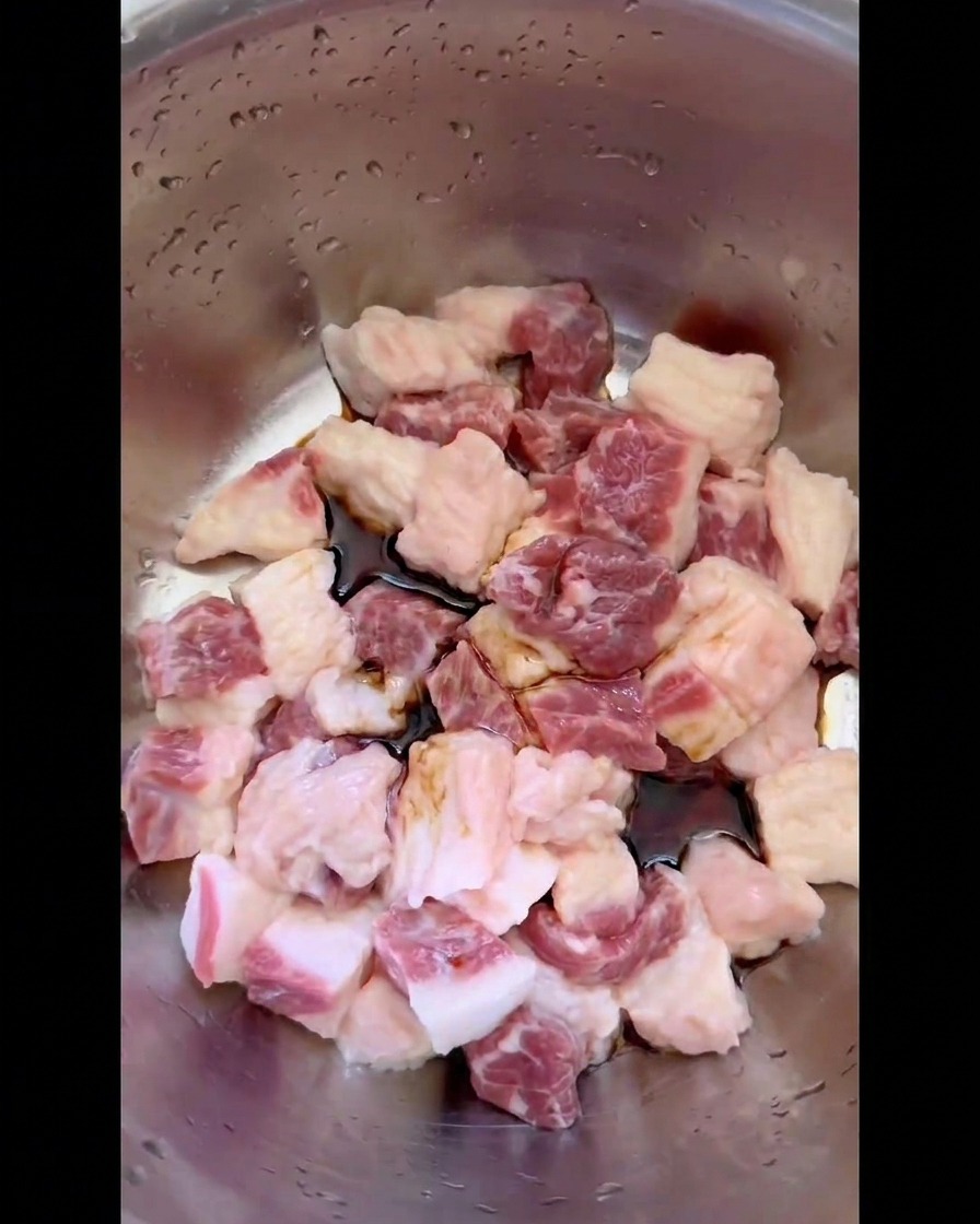 Salsa di soia scura e condimenti liquidi versati sui cubetti di grasso di manzo sul fondo di una ciotola dacciaio.