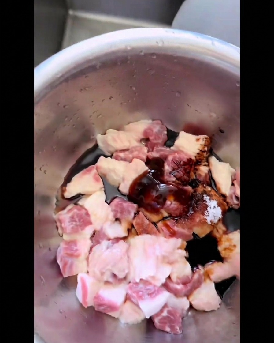 Pezzi di grasso di manzo mescolati a mano con una marinatura scura, zucchero e sale in una ciotola.