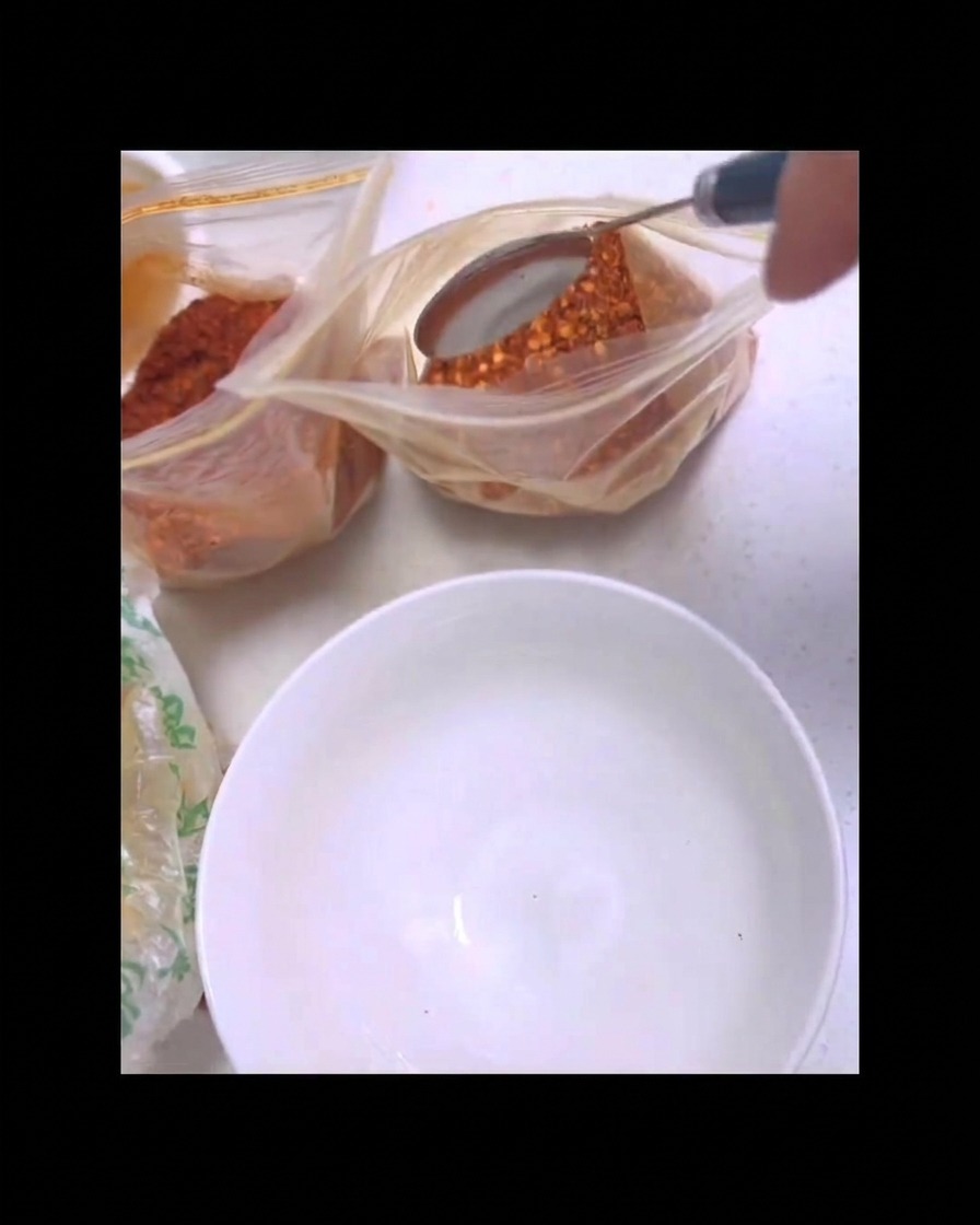 Un cucchiaio di metallo raccoglie la polvere di peperoncino rosso da un sacchetto per versarla in una ciotolina bianca.