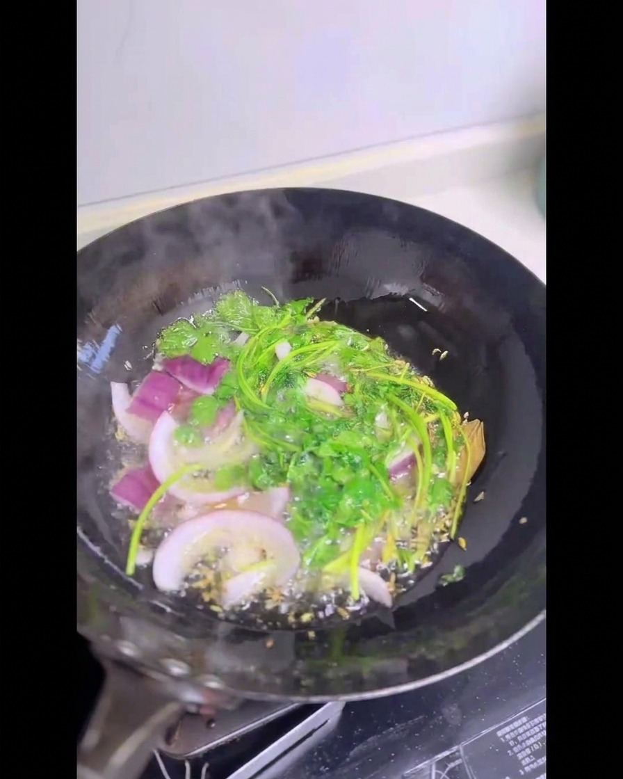 Gambi di coriandolo fresco e fette di cipolla rossa che sfrigolano in un wok colmo di olio caldo.