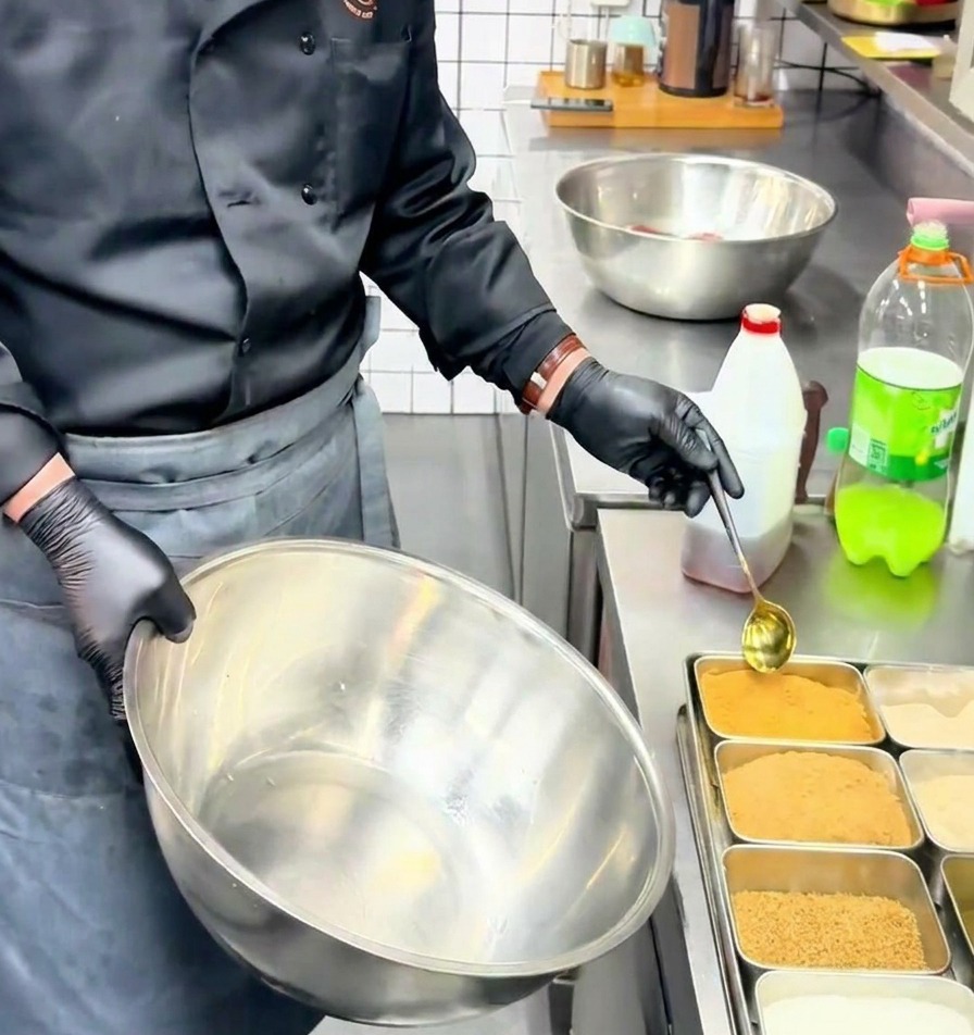 Uno chef usa un cucchiaio dorato per versare linsaporitore di manzo in polvere in una grande ciotola in acciaio inossidabile.