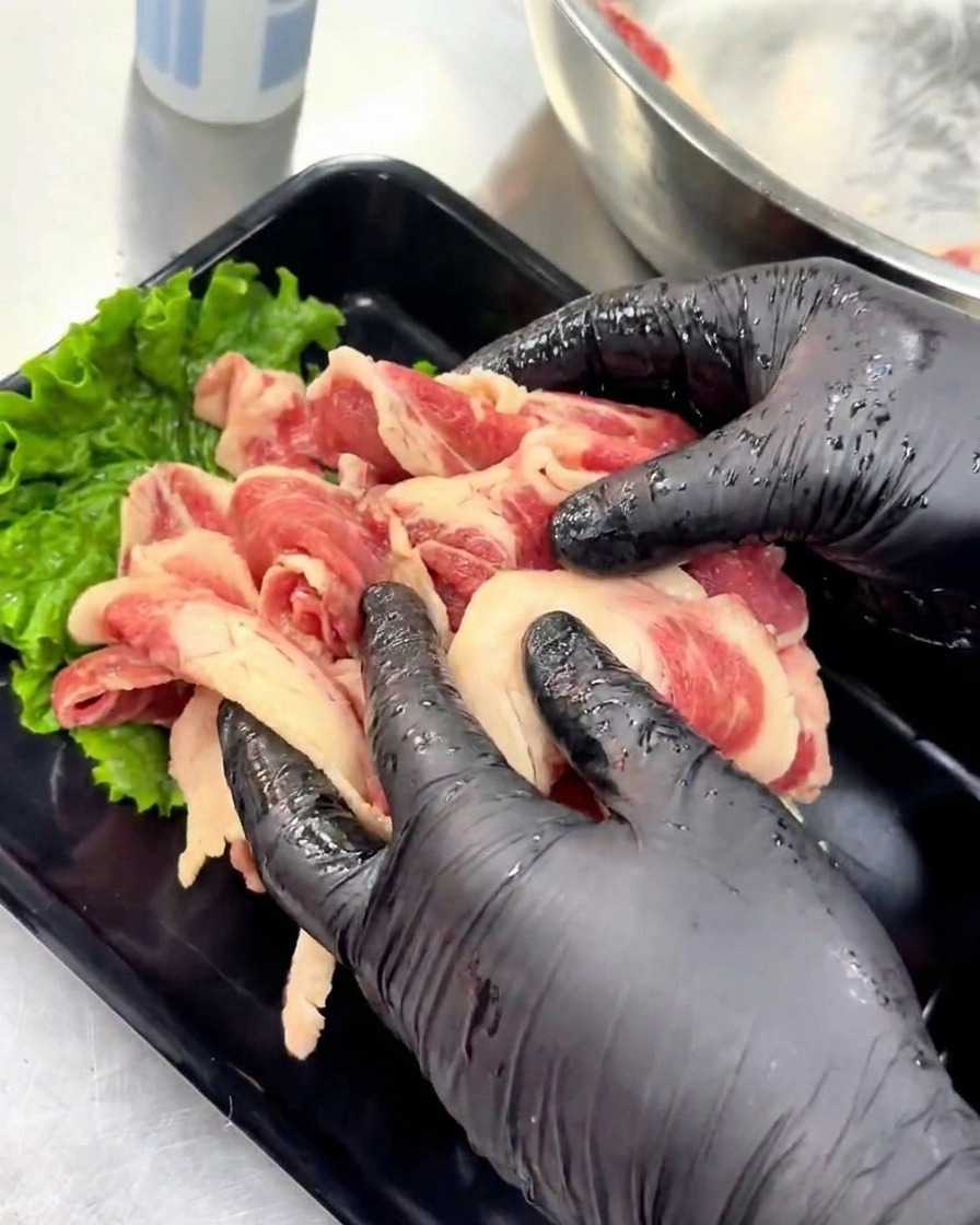 Mani con guanti dispongono ordinatamente le fette di manzo crudo marinato su un vassoio da portata nero decorato con una foglia di lattuga verde.