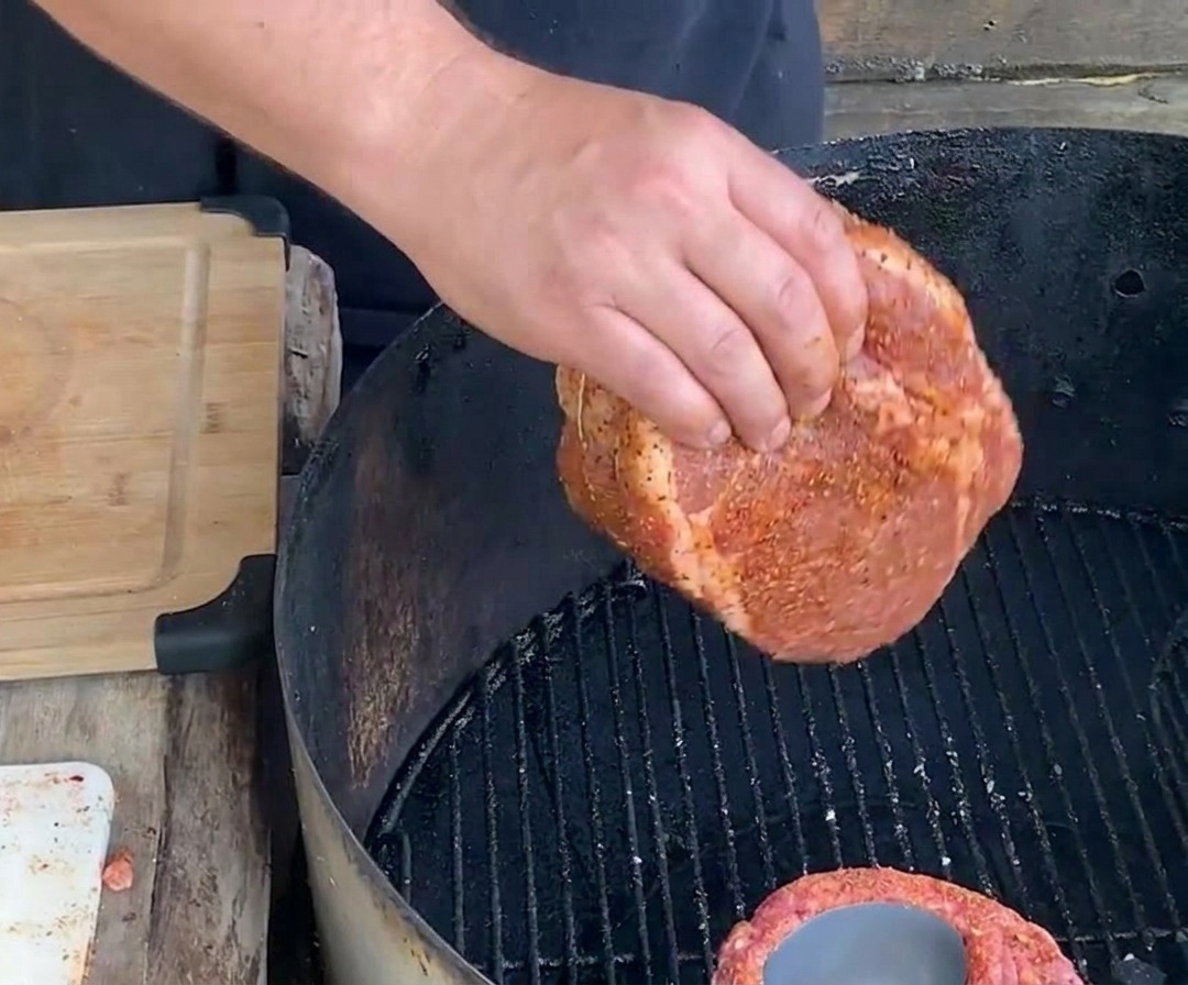 Una mano adagia un cestino di costine cilindrico condito e legato, con la lattina ancora allinterno, sulla griglia dacciaio nera di un barbecue a carbone per una cottura lenta.