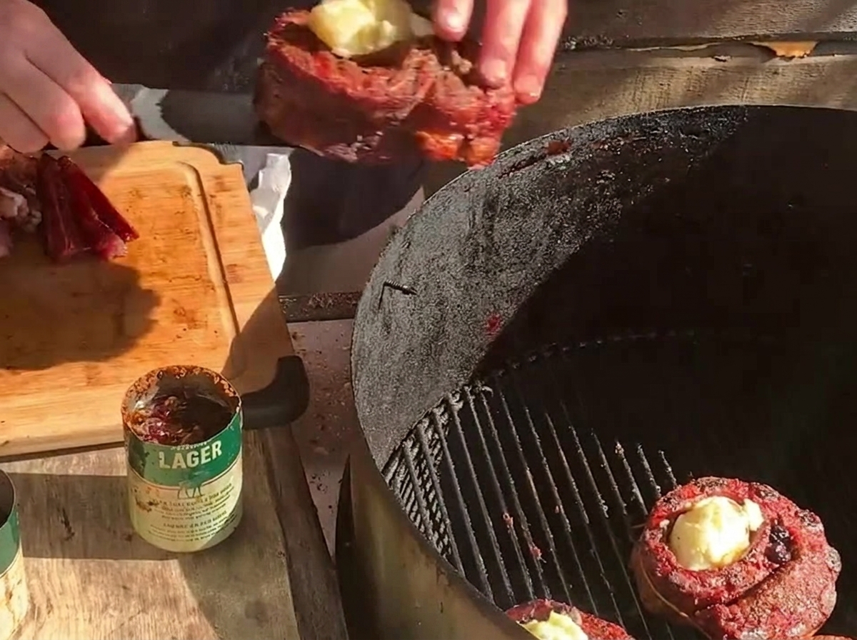 Un cestino di costine farcito viene riposizionato su un barbecue a carbone accanto a un altro cestino di carne e a fette spesse di bacon.