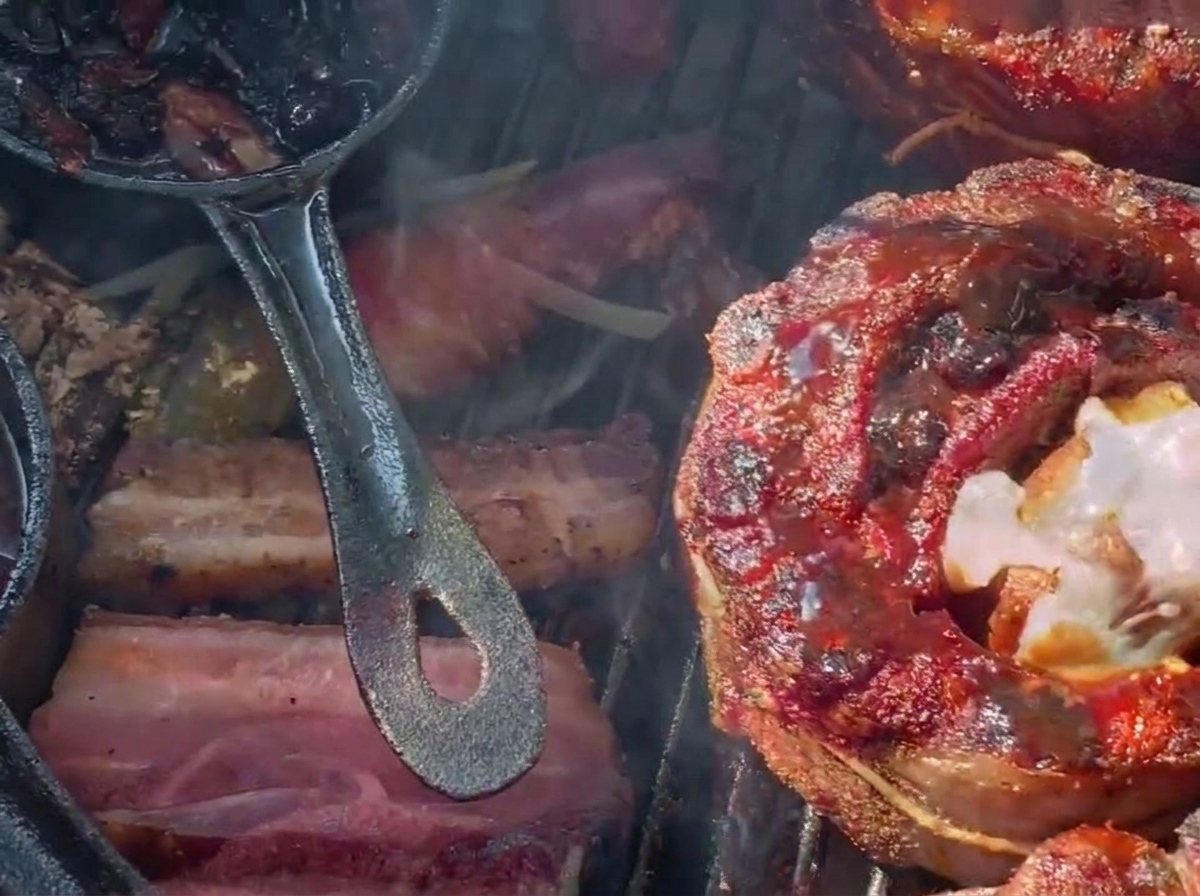 Formaggio grattugiato che si scioglie sopra un cestino di costine farcito scuro e glassato ai mirtilli su un barbecue a carbone.