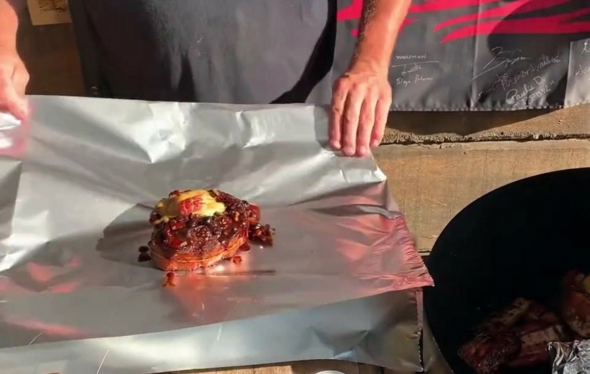 Un cestino di costine St. Louis completamente farcito, coperto di formaggio e salsa, posizionato su un foglio di alluminio pronto per essere avvolto.