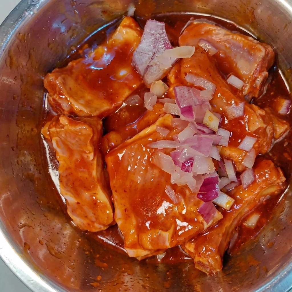 Cipolla rossa tritata finemente cosparsa sulle costine di maiale crude marinate in una ciotola di metallo.