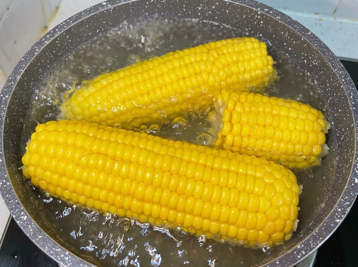 Pannocchie di mais dolce giallo che bollono in una pentola dacqua sul fuoco in cucina.