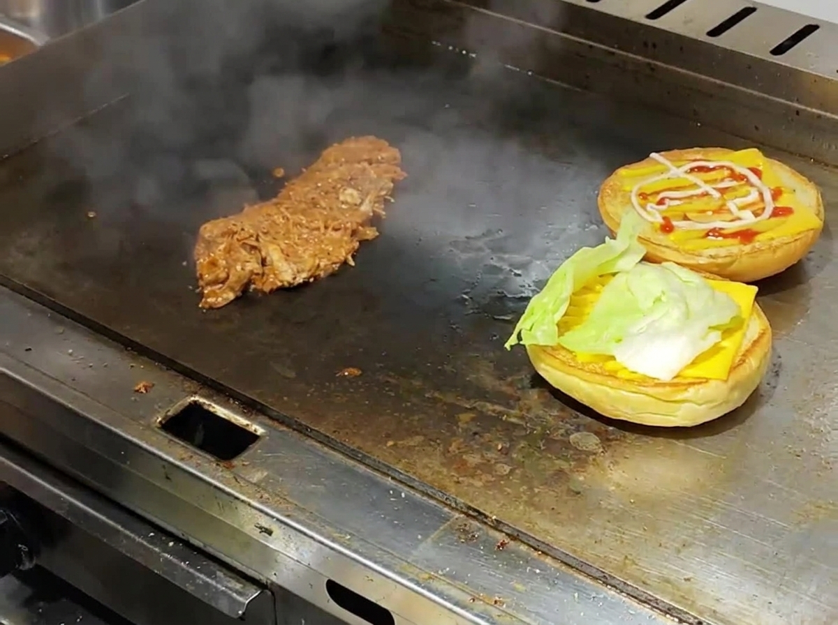 Panini da burger tostati conditi con formaggio e lattuga accanto al pulled pork caldo su una piastra da cucina.