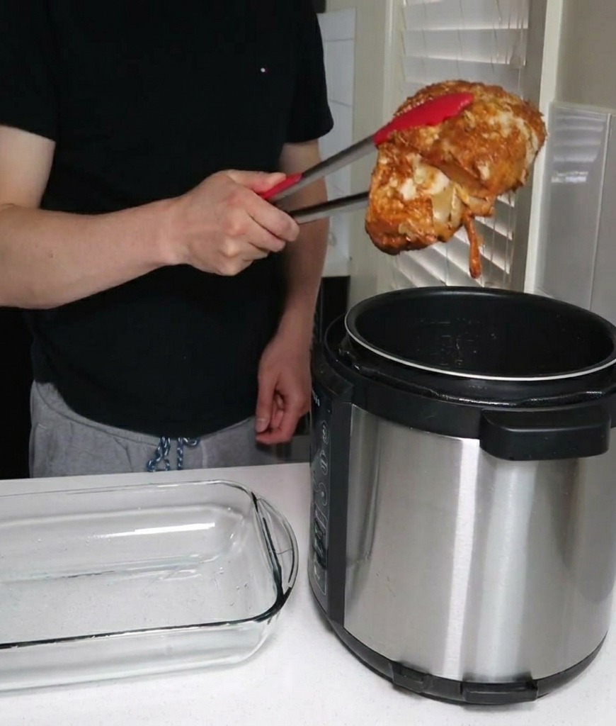 Una persona solleva un grosso pezzo di spalla di maiale cotta dalla pentola a pressione usando delle pinze da cucina, spostandola verso una pirofila in vetro vuota.