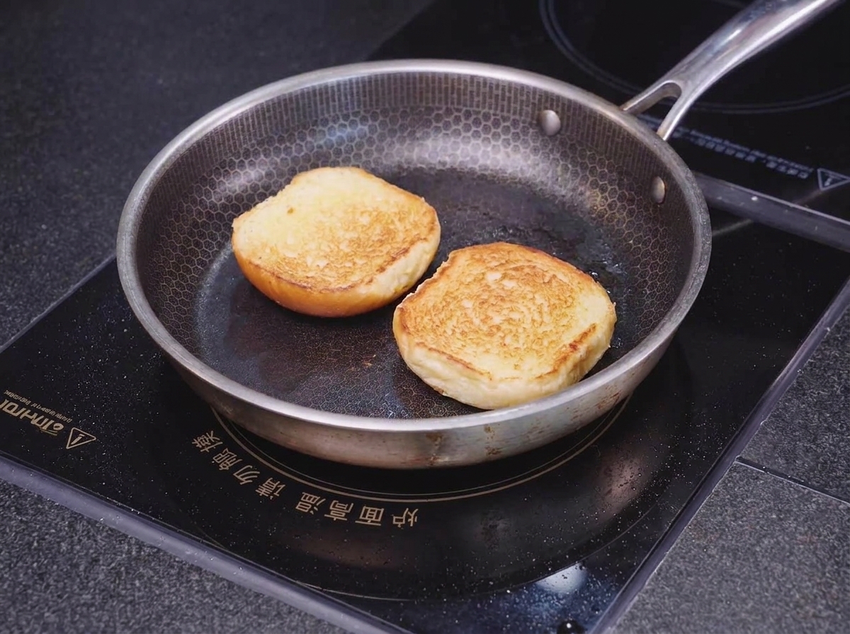 Due metà di un panino brioche che si tostano rivolte verso il basso in una padella con trama a nido dape fino a doratura dei bordi.