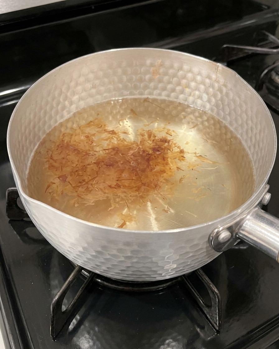 Leggeri fiocchi di katsuobushi color ambra che galleggiano sulla superficie del brodo caldo in una pentola.
