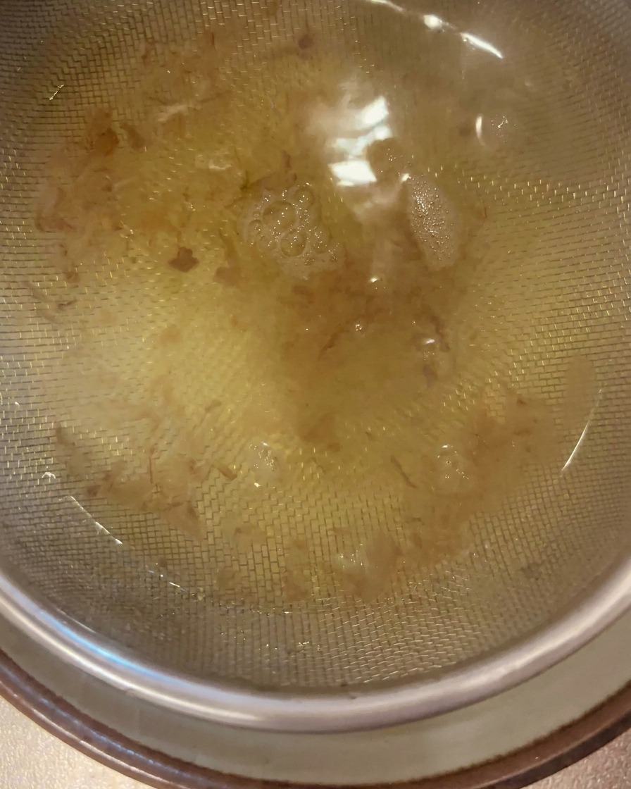 Un limpido brodo dashi dorato viene filtrato attraverso un colino a maglia fine in acciaio inossidabile dentro una ciotola.