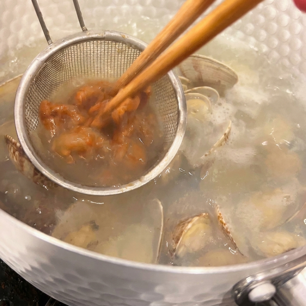 Un piccolo colino immerso nella zuppa calda contiene la pasta di miso scura mentre viene stemperata con laiuto di bacchette.