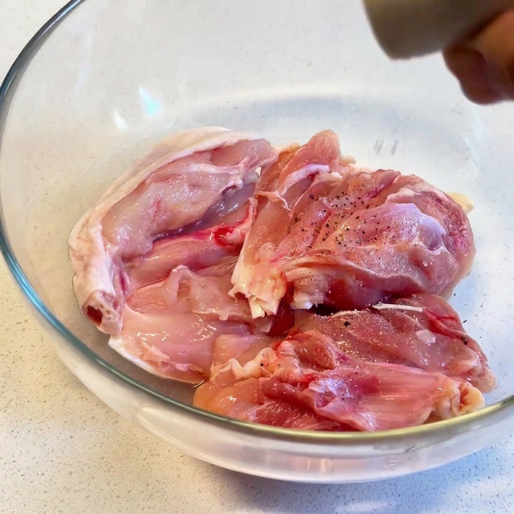 Sovracosce di pollo crude in una ciotola di vetro trasparente, insaporite con pepe nero macinato fresco.