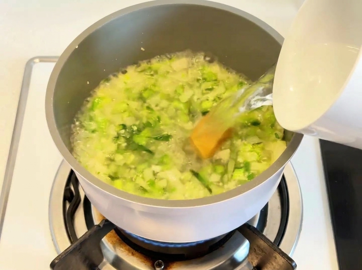 Acqua versata in una pentola contenente verdure saltate e dado da brodo.