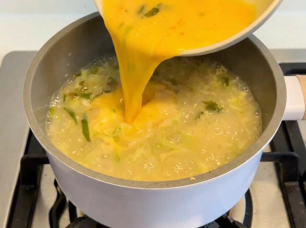 Un composto di un giallo vivace a base di uova e limone versato da una ciotola bianca in una pentola di zuppa cremosa.