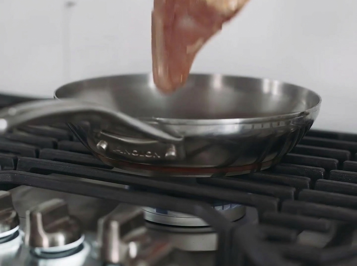 Un petto di pollo che scotta in una padella di acciaio inossidabile sul piano cottura.