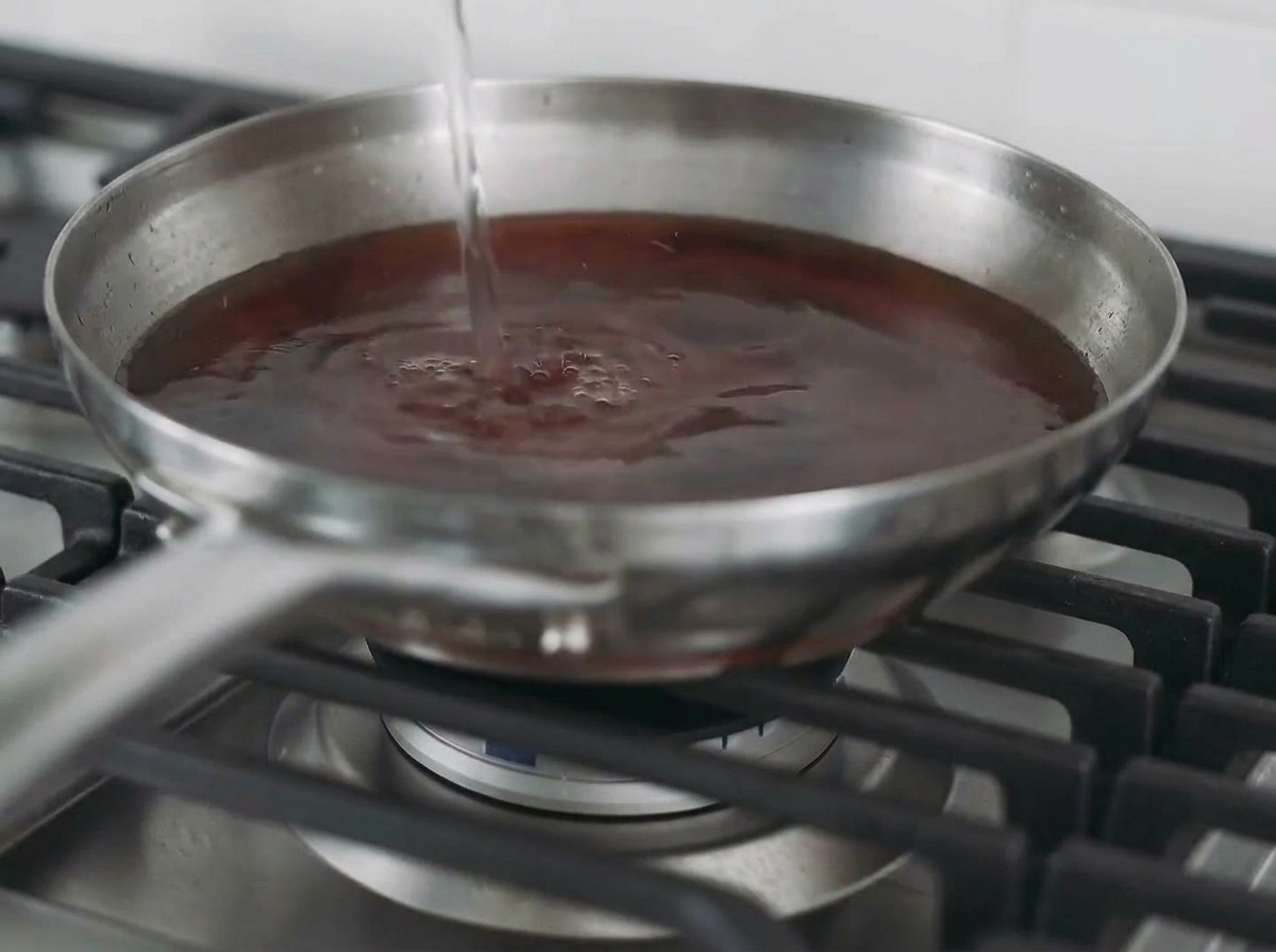 Liquido versato in una padella contenente un petto di pollo scottato per creare un brodo.